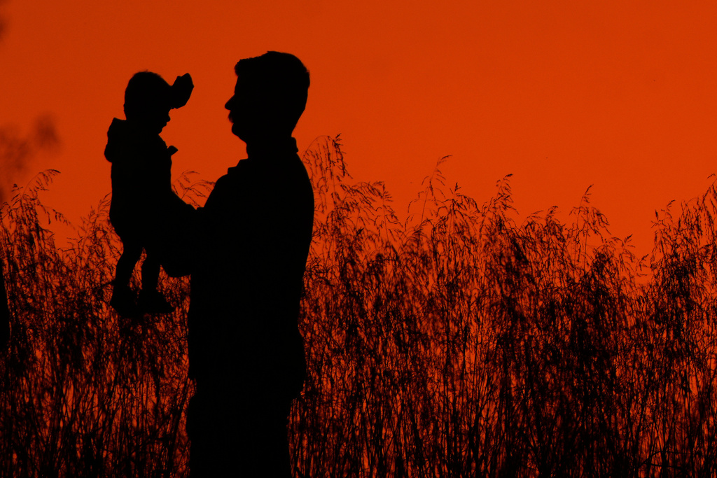 A man holds up a child while walking in a park at sunset, Wednesday, Oct. 15, 2025, in Shawnee, Kan. (AP Photo/Charlie Riedel)