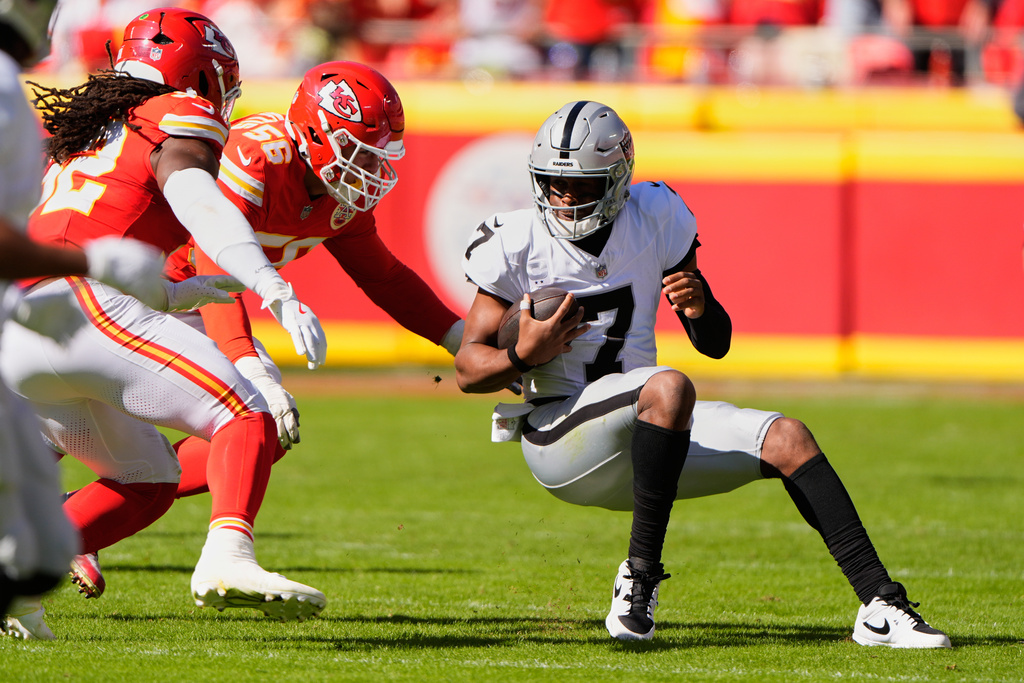 Las Vegas Raiders quarterback Geno Smith (7) scrambles as Kansas City Chiefs defensive end George Karlaftis (56) and linebacker Nick Bolton, left, defend during the first half of an NFL football game Sunday, Oct. 19, 2025, in Kansas City, Mo. (AP Photo/Charlie Riedel)