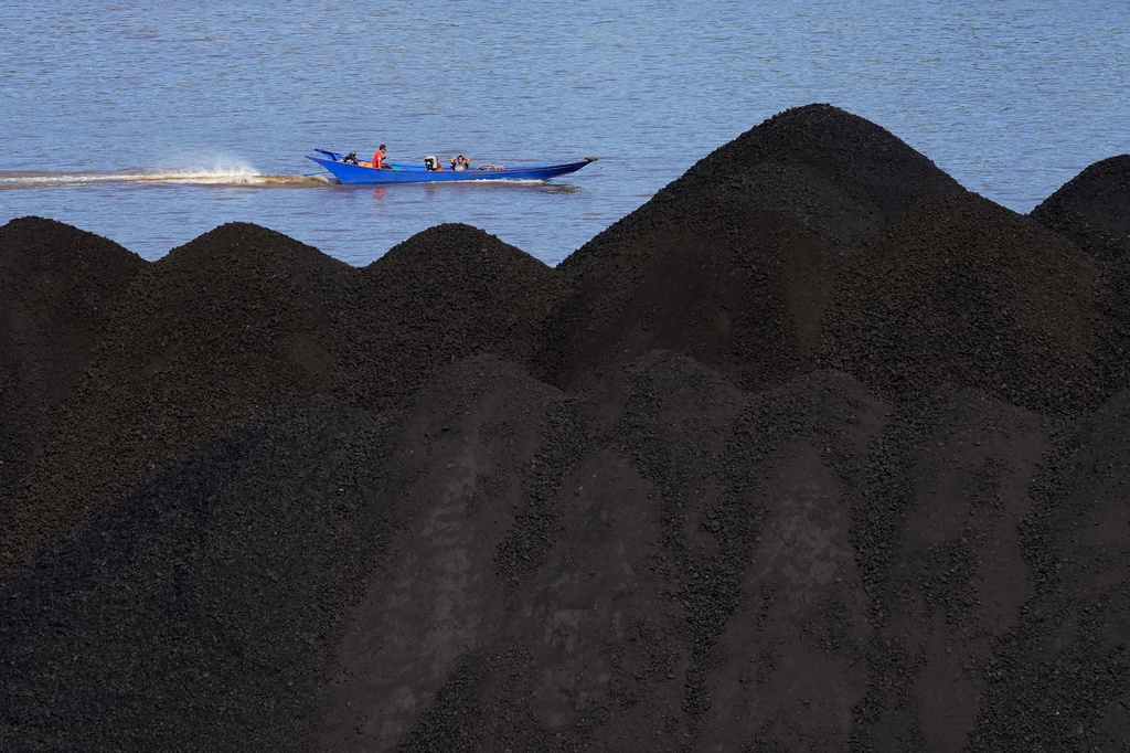 FILE - A boat cruises past a coal piled up on a barge on Mahakam River in Samarinda, East Kalimantan, Indonesia, Dec. 19, 2022. (AP Photo/Dita Alangkara, File)