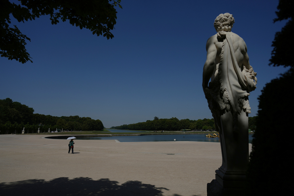 A woman shields herself from the sun with an umbrella as she walks in the garden of the Palace of Versailles, outside Paris, during a heat wave with temperatures soaring above 40 degrees Celsius (104 Fahrenheit), Monday, June 22, 2026. (AP Photo/Thibault Camus)