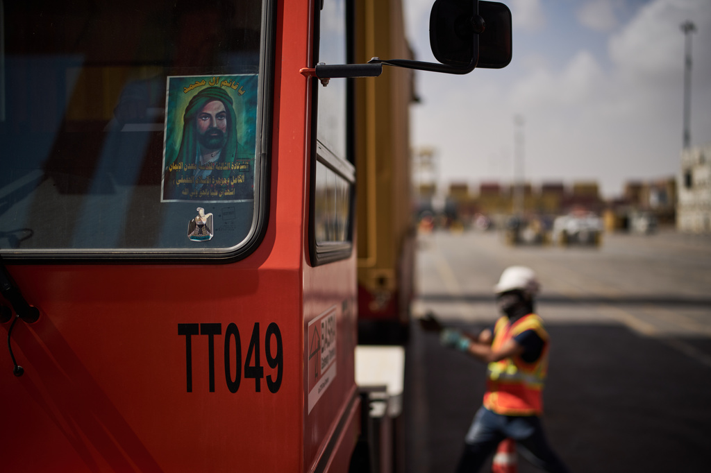 An image depicting Ali ibn Abi Talib, the cousin and son-in-law of the Prophet Muhammad, who is revered by Muslims particularly Shiite sect, is displayed on the windshield of a truck as dockworkers unload cargo containers at Umm Qasr Port, a deep-water port, in the city of Umm Qasr, Iraq, Friday, March 27, 2026. (AP Photo/Leo Correa)