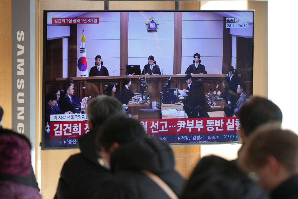 A TV screen shows a live footage of Kim Keon Hee, the wife of South Korea's former President Yoon Suk Yeol, second from right, wearing a mask, during a news program, at the Seoul Railway Station in Seoul, South Korea, Wednesday, Jan. 28, 2026. (AP Photo/Lee Jin-man)