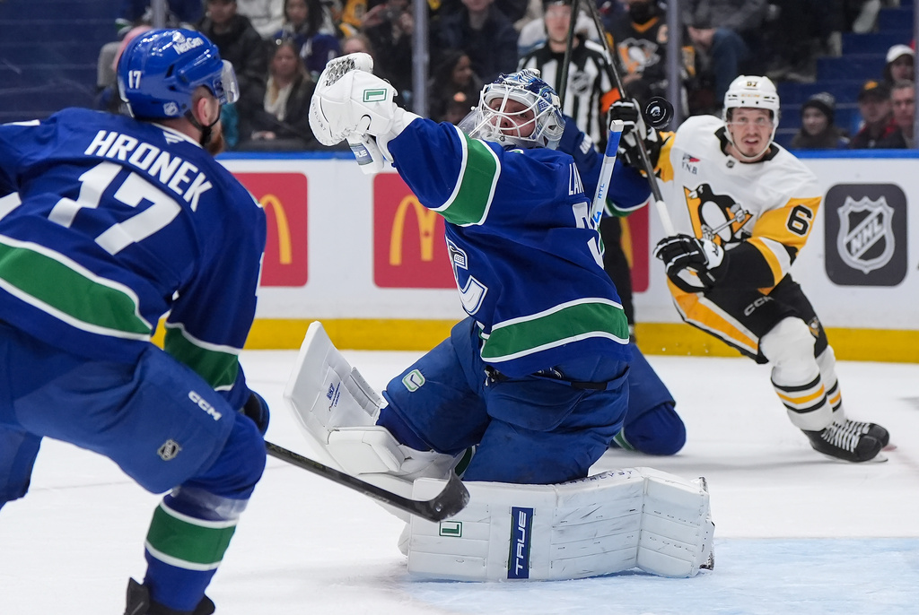 Vancouver Canucks goalie Kevin Lankinen, cener, fails to catch the puck as teammate Filip Hronek (17) and Pittsburgh Penguins' Rickard Rakell (67) watch during first-period NHL hockey game action in Vancouver, British Columbia, Sunday, Jan. 25, 2026. (Darryl Dyck/The Canadian Press via AP)