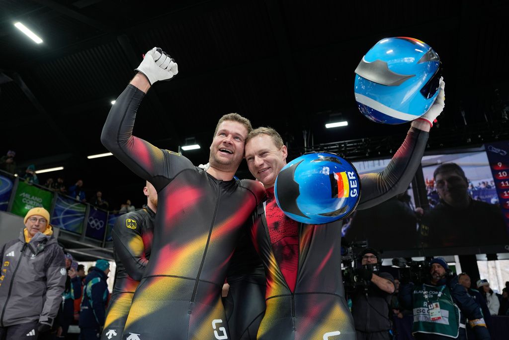Germany's gold medalists Johannes Lochner, left, and Germany's silver medalist Francesco Friedrich, right, celebrate at the finish after the four man bobsled competition at the 2026 Winter Olympics, in Cortina d'Ampezzo, Italy, Sunday, Feb. 22, 2026. (AP Photo/Alessandra Tarantino)