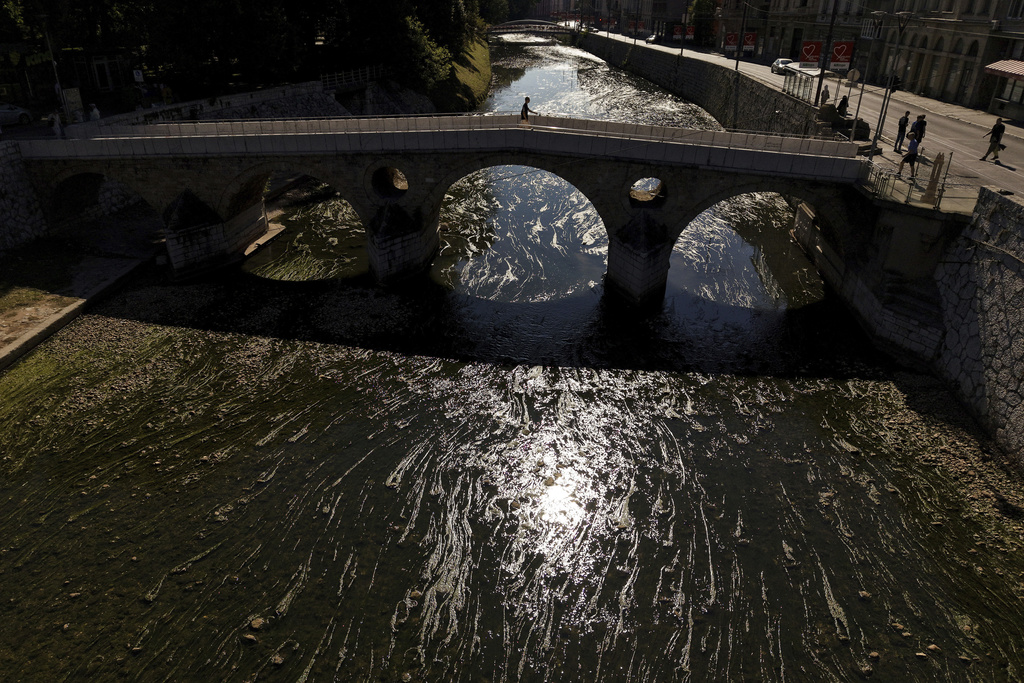 A pedestrian walks across a bridge over the Miljacka River, nearly dried up and covered with algae, amid a heat wave and drought in Sarajevo, Bosnia, Aug. 10, 2025. (AP Photo/Armin Durgut)