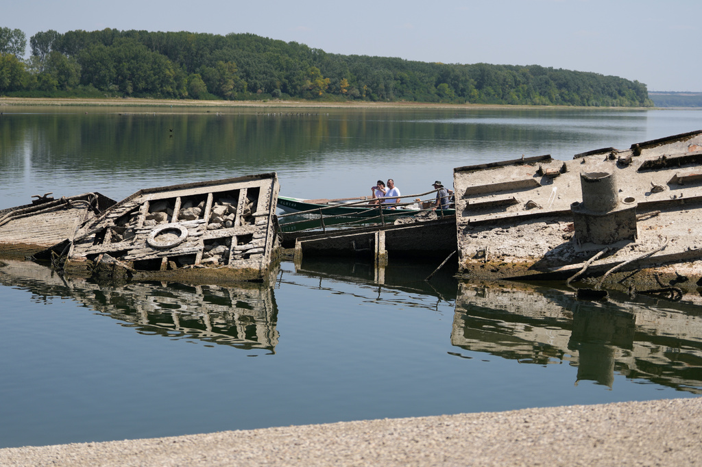 People watch the wreckage of a WWII German warship, emerged due to the drought, in front of Djerdap II, a large dam on the Danube River, between Romania and Serbia, near Prahovo, Serbia, Tuesday, Aug. 4, 2026. (AP Photo/Darko Vojinovic)