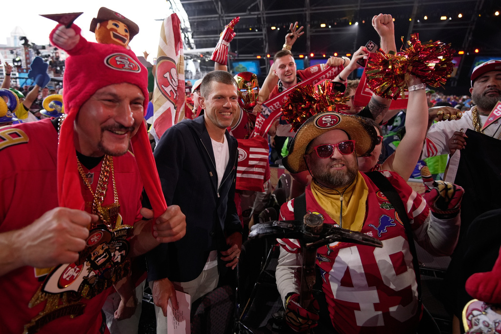 Former NFL player Andy Lee, center, poses with San Francisco 49ers fans during the second round of the NFL football draft, Friday, April 24, 2026, in Pittsburgh. (AP Photo/Sue Ogrocki)