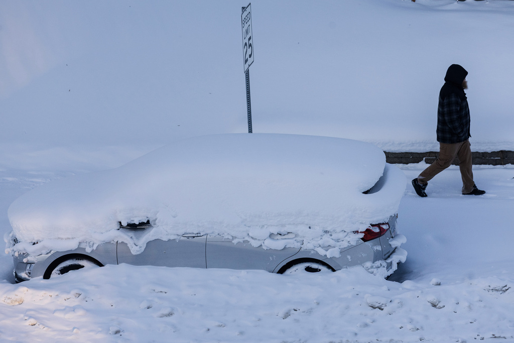 A person walks by a vehicle that was plowed in by snow in Grand Rapids, Mich. on Friday, Jan. 23, 2026. (Joel Bissell/Kalamazoo Gazette via AP)