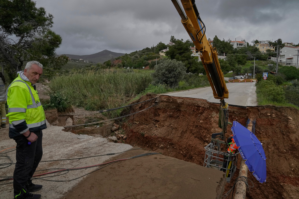 Utility workers repair a water pipe at a road cut in two, in Kallitechnoupoli suburb of Athens, on Thursday, April 2, 2026, after heavy overnight storms caused extensive damage. (AP Photo/Thanassis Stavrakis)