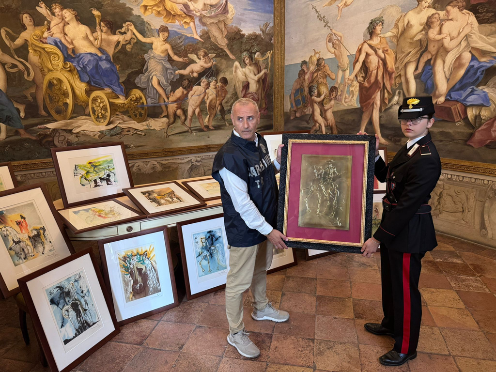 In this handout photo released Wednesday, Oct. 1, 2025 by Italy's Carabinieri Cultural Heritage Protection Command, two officers pose with some of the 21 artworks from the exhibition "Dali. Between Art and Myth" that were seized on suspicion of being fakes, in Parma, northern Italy, Tuesday, Sept. 30, 2025. (Carabinieri Cultural Heritage Protection Command via AP)