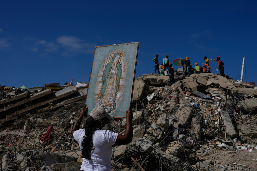 A woman holds a painting of the Virgin Mary as she accompanies a Catholic priest supporting people searching for the remains of relatives in the rubble of residential buildings that collapsed during the earthquakes that struck La Guaira, Venezuela, Friday, July 17, 2026. (AP Photo/Ariana Cubillos)