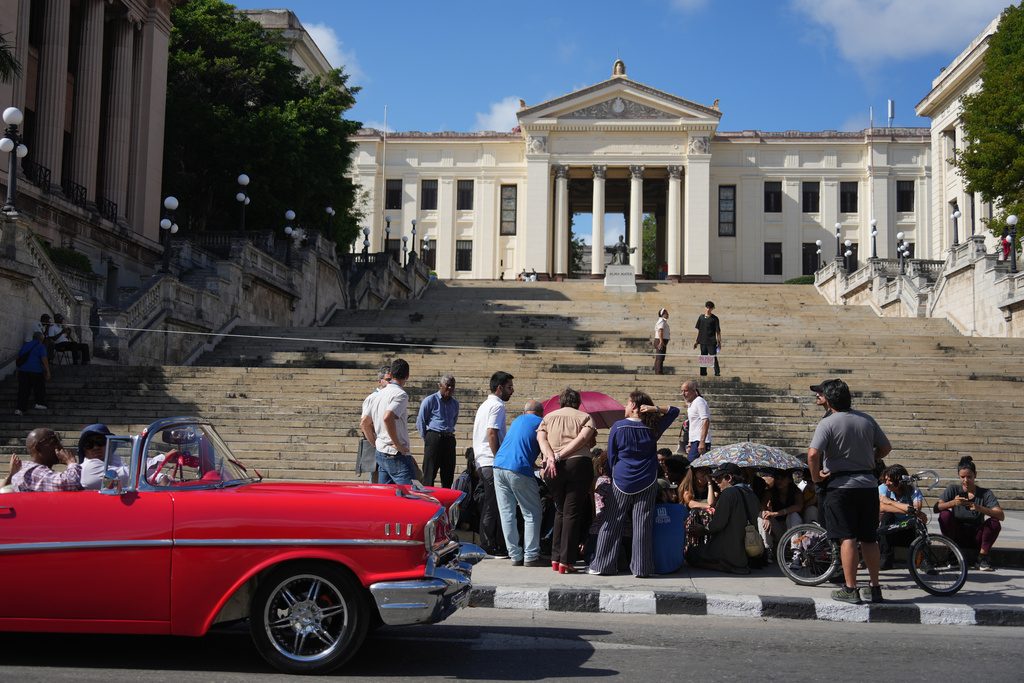A car rides past students sitting outside the University of Havana during a protest over an energy crisis that has disrupted classes in Havana, Cuba, Monday, March 9, 2026. (AP Photo/Ramon Espinosa)