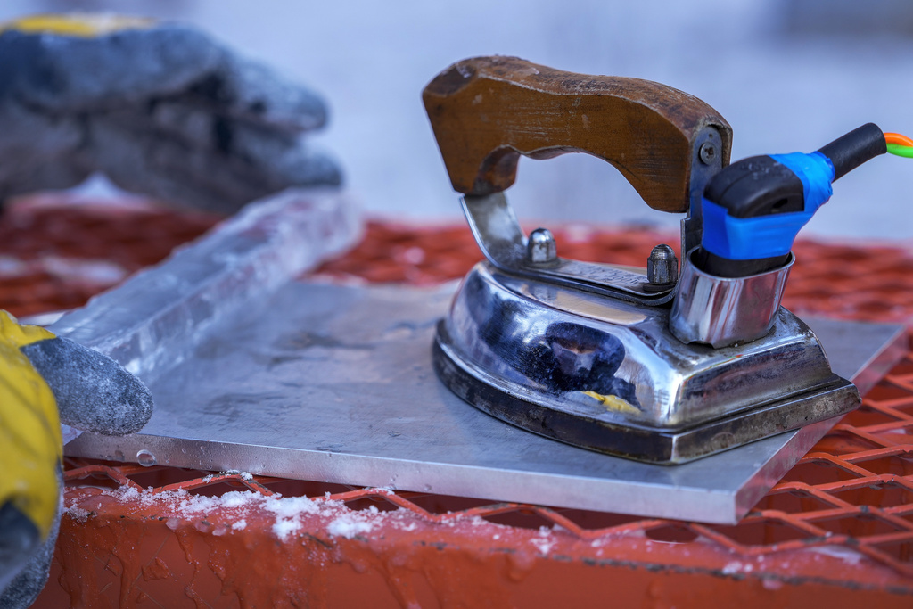 An artist is reflected on an iron as he works on an ice block during the National Professional Ice Sculpture Contest at the Harbin Ice and Snow World in Harbin, China's Heilongjiang province on Wednesday, Jan. 8, 2025. (AP Photo/Andy Wong)