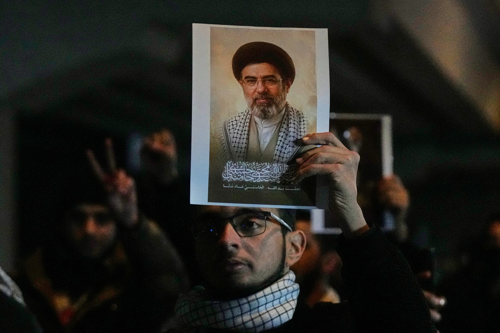 Iraqis hold a portrait of the new successor to Supreme Leader, Ayatollah Mojtaba Khamenei at a bridge leading to the fortified Green Zone where the U.S. embassy is located in Baghdad, Iraq, Monday, March 9, 2026. (AP Photo/Hadi Mizban)