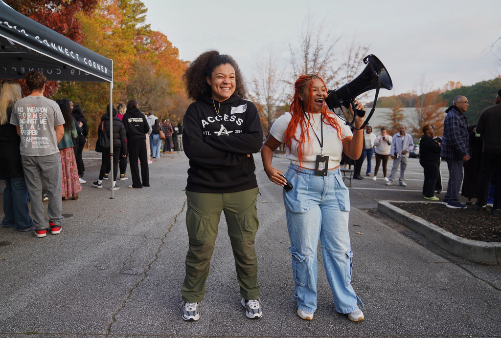 Brandi Porter, left, and Kennedy Onley, right, engage in a call and response with churchgoers as they wait in line on Nov. 16, 2025, in Atlanta. (AP Photo/Jessie Wardarski)