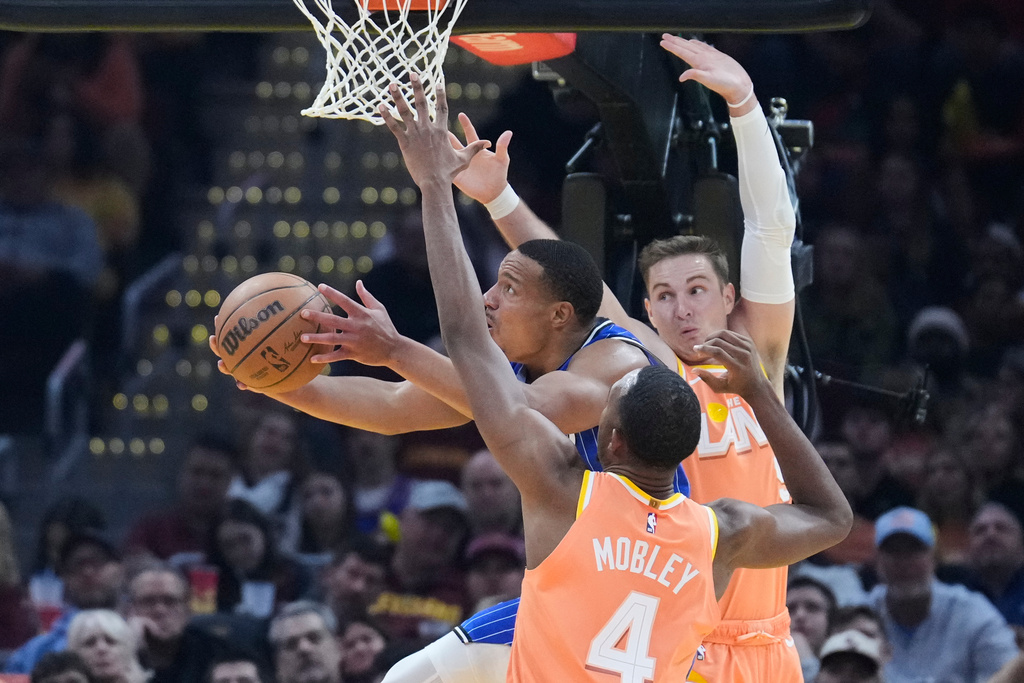 Orlando Magic guard Desmond Bane, left, goes to the basket between Cleveland Cavaliers center Evan Mobley (4) and guard Sam Merrill, right, in the first half of an NBA basketball game in Cleveland, Tuesday, March 24, 2026. (AP Photo/Sue Ogrocki)