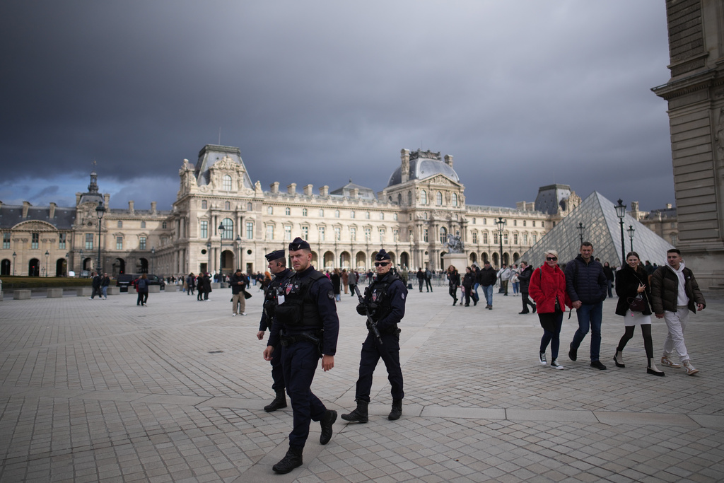 Riot police officers patrol as people stroll in Le Louvre museum courtyard, Monday, Oct. 27, 2025 in Paris. (AP Photo/Christophe Ena)