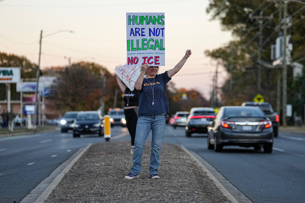 Protesters holds signs amidst the arrival of federal law enforcement, Monday, Nov. 17, 2025, in Charlotte, N.C. (AP Photo/Matt Kelley)