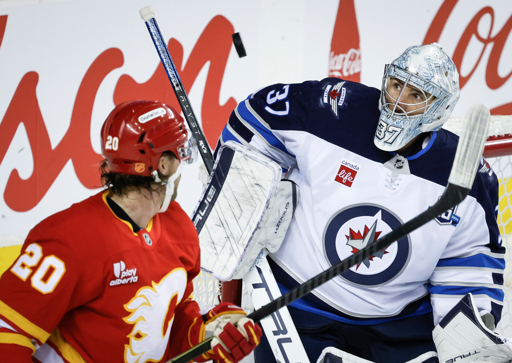 Winnipeg Jets goalie Connor Hellebuyck, right, keeps his eyes on the puck as Calgary Flames' Blake Coleman looks on during third period NHL hockey action in Calgary, Alta., Monday, Oct. 20, 2025. (Jeff McIntosh/The Canadian Press via AP)