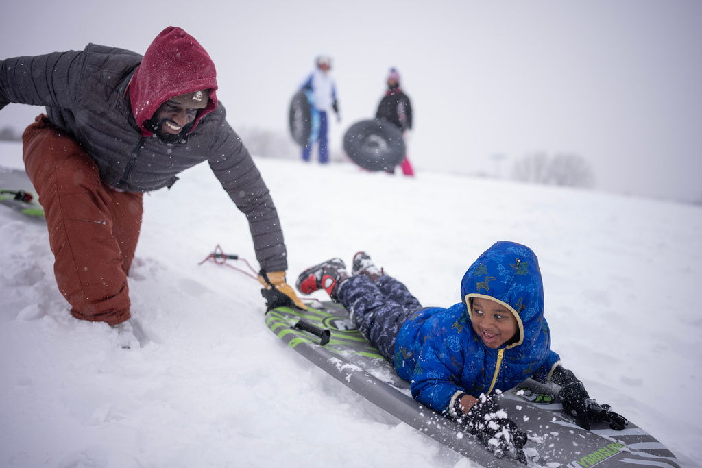 Ogo Akpati and his son Brycson Akpati, 3, braved the strong winds and had fun sliding down a hill in Central Park Sunday, March 15,2026 in Brooklyn Park, MN. (Jerry Holt/Minnesota Star Tribune via AP)