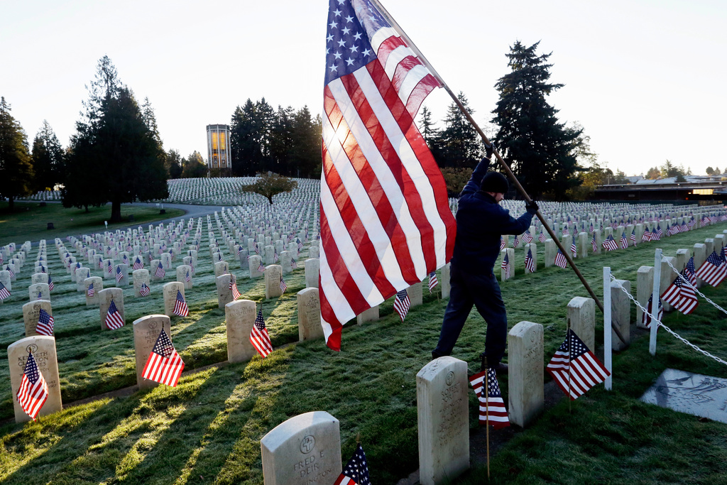 FILE - A larger American flag is raised among flag-covered graves on Veterans Day in the veterans' section of Evergreen-Washelli cemetery, on Nov. 11, 2014, in Seattle. (AP Photo/Elaine Thompson)