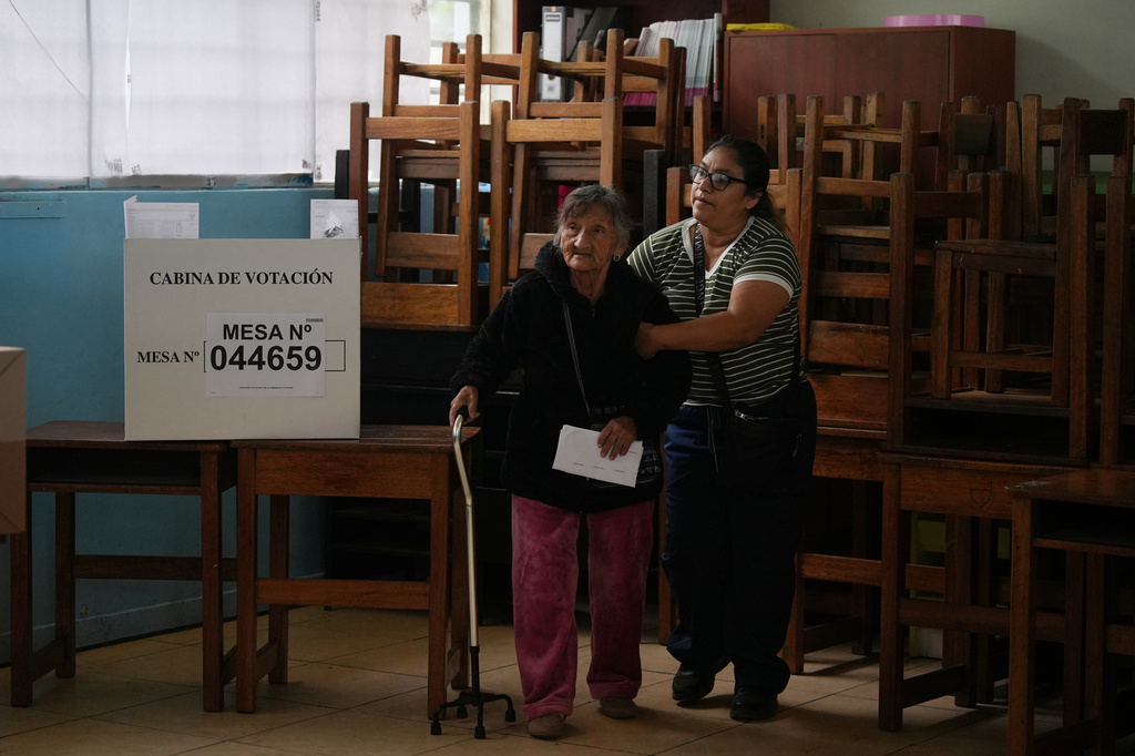 A relative helps a woman vote as polling resumes at a station affected by delays and logistical problems during general elections in Lima, Peru, Monday, April 13, 2026. (AP Photo/Guadalupe Pardo)