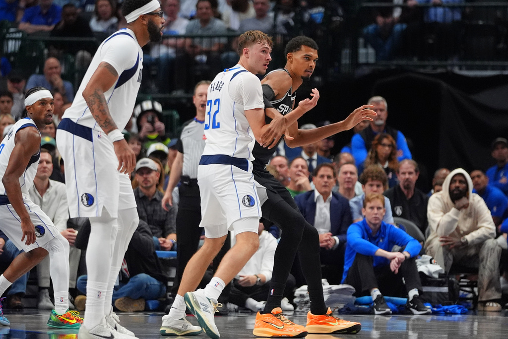 San Antonio Spurs forward Victor Wembanyama, right, is defended by Dallas Mavericks forward Cooper Flagg (32) as forward Anthony Davis, second from left, looks on during the second half of an NBA basketball game in Dallas, Wednesday, Oct. 22, 2025. (AP Photo/LM Otero)