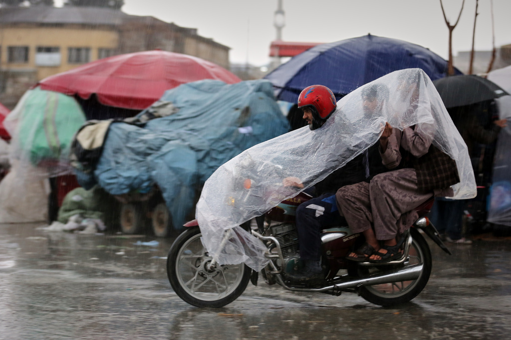 A man rides a motorcycle with two passengers under a plastic cover through heavy rain in Kabul, Afghanistan, Tuesday, March 31, 2026. (AP Photo/Siddiqullah Alizai)