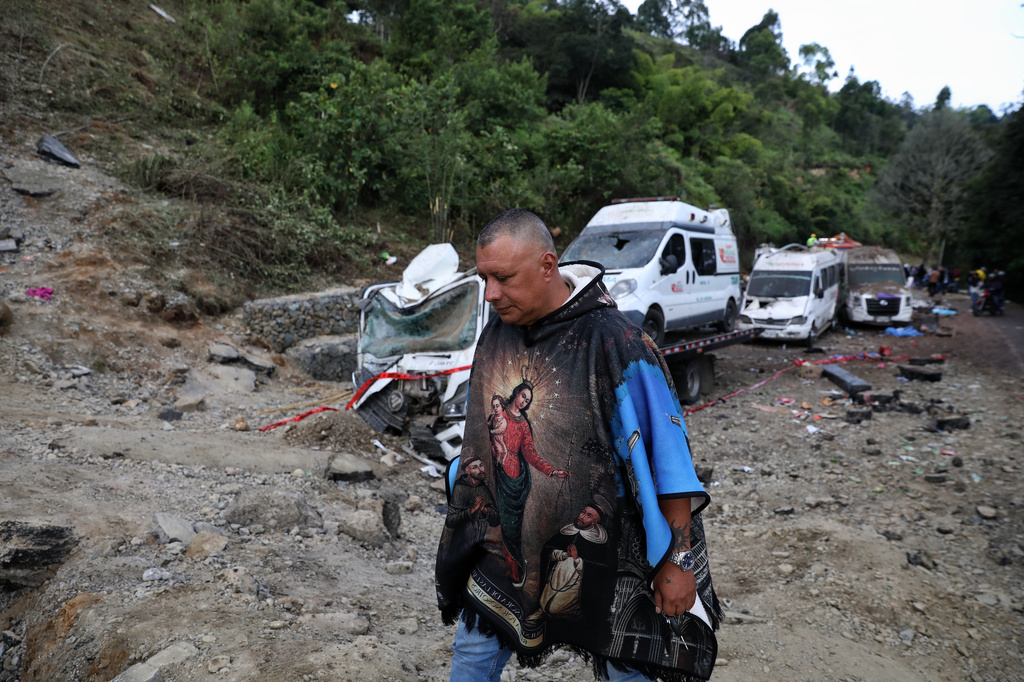 A man walks past vehicles damaged in an attack on the Pan-American Highway in Cajibio, Colombia, Sunday, April 26, 2026, where at least a dozen people were killed in an attack authorities blamed on dissident groups of the former FARC rebels. (AP Photo/Santiago Saldarriaga)
