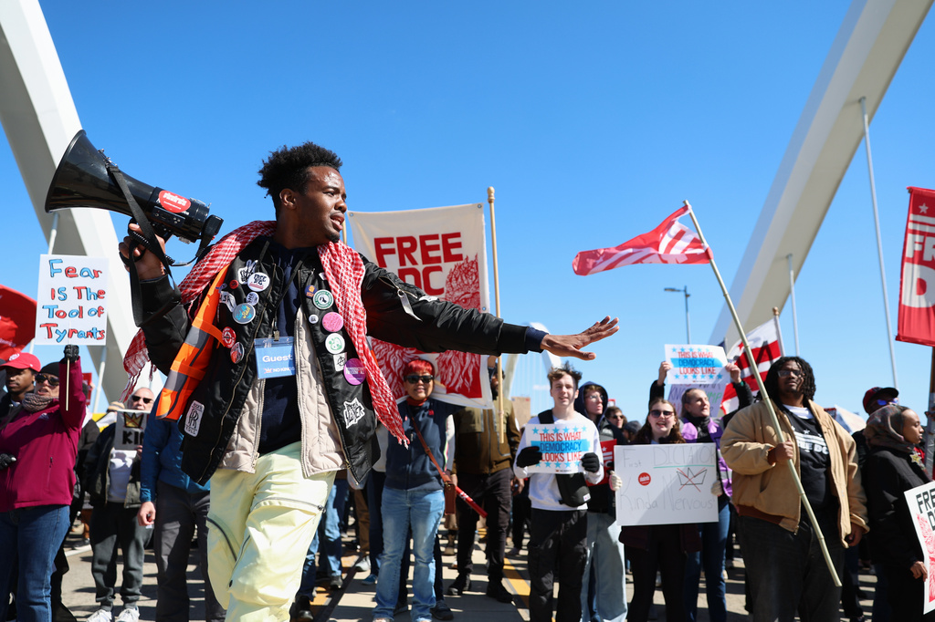 Demonstrators march over the Frederick Douglass Bridge during the No Kings protest in Washington, Saturday, March 28, 2026. (AP Photo/Tom Brenner)