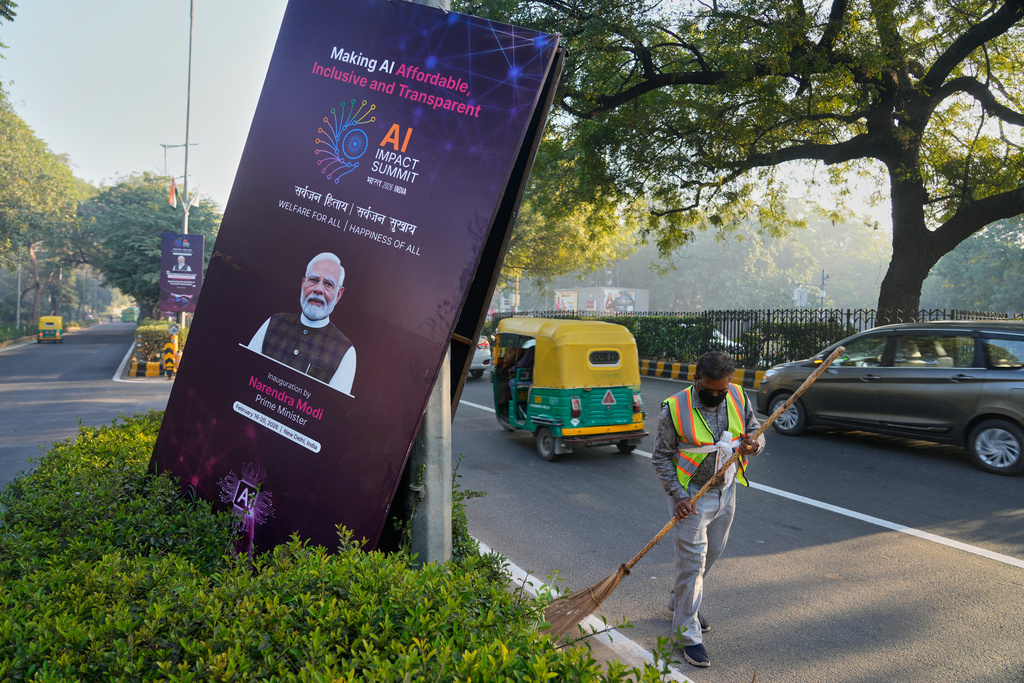 A municipal worker sweeps on a street with banners of the AI-Summit with Indian Prime Minister Narendra Modi photographs in New Delhi, India, Monday, Feb. 16, 2026. (AP Photo/Manish Swarup)