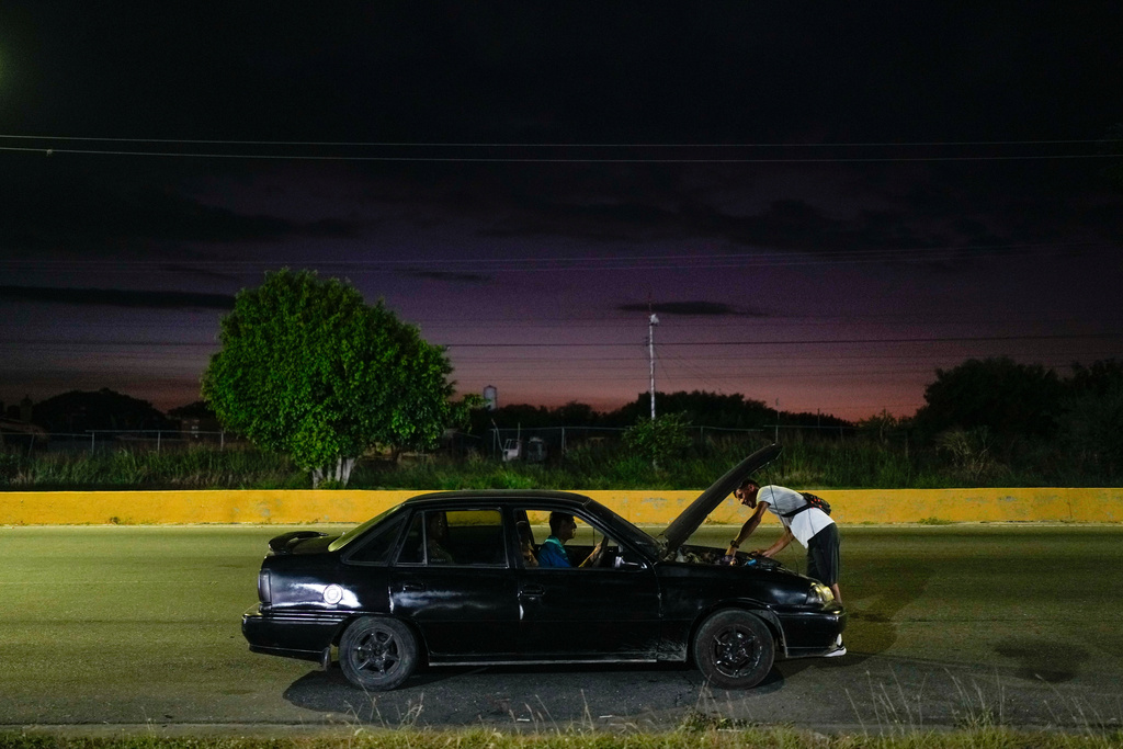 Abraham Castro helps fix the taxi taking him and his partner, Mariela Gómez, to his parents' home for Christmas dinner in Maracay, Venezuela, Wednesday, Dec. 24, 2025. The Venezuelan migrant couple abandoned their journey to the United States and returned home from Mexico by land and sea following the immigration crackdown under President Donald Trump. (AP Photo/Matias Delacroix)