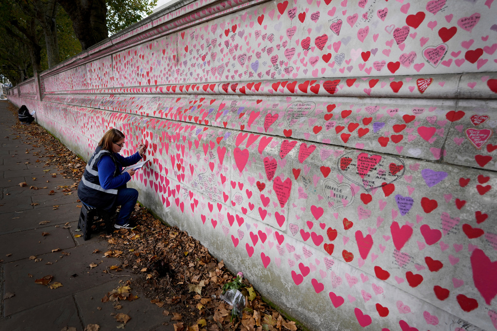 FILE - Volunteer Amanda Herring who lost her brother Mark to COVID-19, writes inscriptions on the COVID-19 memorial wall in Westminster in London, Friday, Oct. 15, 2021. (AP Photo/Kirsty Wigglesworth, File)