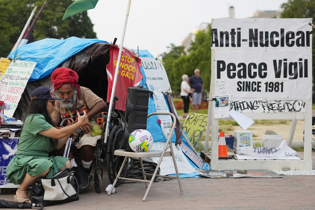 Philipos Melaku-Bello, second from left, looks over a passerbys phone while at the White House Peace Vigil in Lafayatte Park across the street from the White House in Washington, Friday, Sept. 5, 2025. (AP Photo/Pablo Martinez Monsivais)