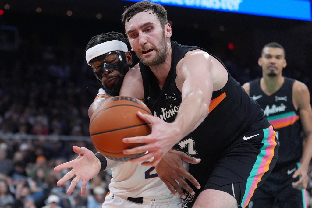 Phoenix Suns guard Jordan Goodwin, left, and San Antonio Spurs center Luke Kornet, right, scramble for a loose ball during the first half of an NBA basketball game in Austin, Texas, Thursday, Feb. 19, 2026. (AP Photo/Eric Gay)