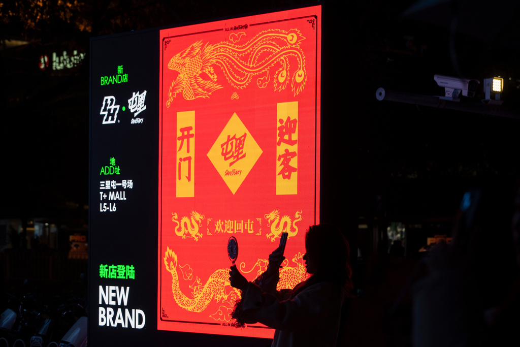 A woman takes a photo near a promotion board at the Taikoo Li Sanlitun mall in Beijing, Wednesday, Oct. 22, 2025. (AP Photo/Ng Han Guan)
