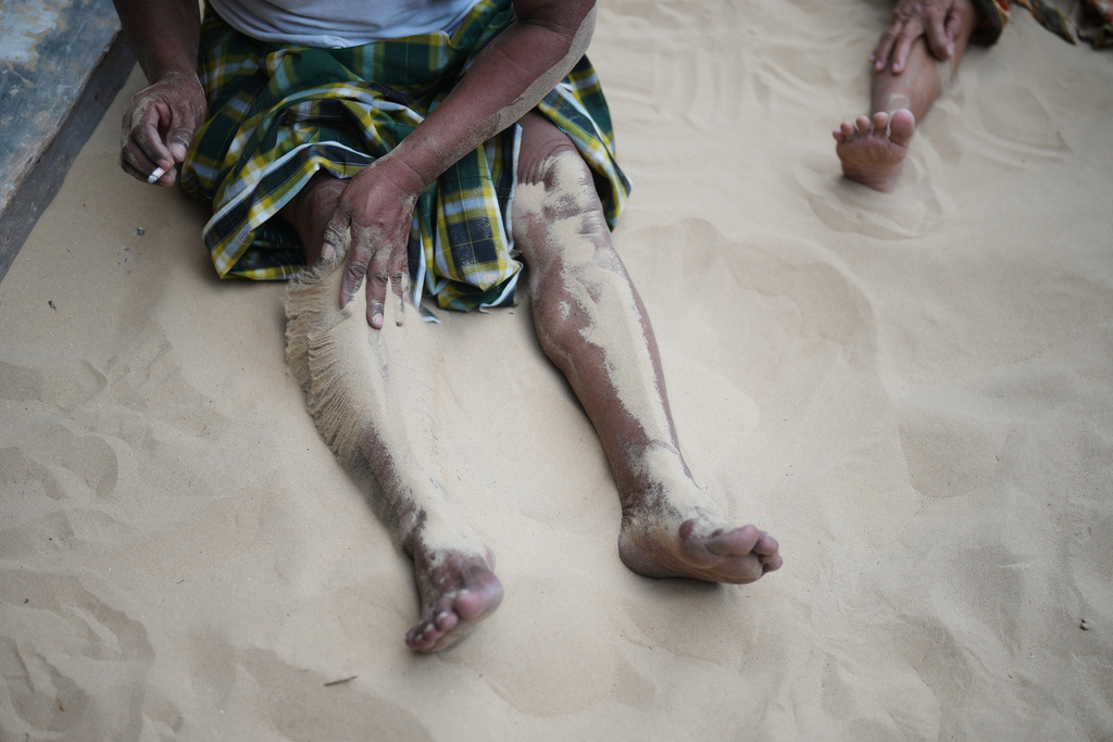 Adnan, one name only, covers his legs with sand in Legung Timur village in Sumenep on Madura Island, Indonesia, Tuesday, Sept. 9, 2025. (AP Photo/Dita Alangkara)
