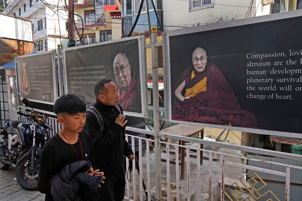 Sonam Tashi, right, and his son, Kunga Tenzin, pass photographs of Tibetan spiritual leader Dalai Lama at the entrance of the Tsuglakhang temple in Mcleodganj near Dharamshala, India, March 6, 2025. (AP Photo/Manish Swarup)