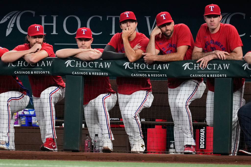 Texas Rangers' Jacob Degrom, from left, MacKenzie Gore, Jack Leiter, Nathan Eovaldi and Cody Bradford, right, stand in the dugout watching play against the San Francisco Giants in the first inning of a baseball game in Arlington, Texas, Monday, Aug. 3, 2026. (AP Photo/Tony Gutierrez)