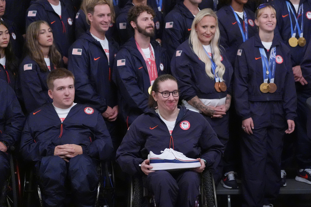 President Donald Trump speaks as alpine monoskier Laurie Stephens, front center, smiles, during an event for Olympic athletes, coaches, staff, and representatives from Team USA in the East Room of the White House, Thursday, Aug. 6, 2026, in Washington. (AP Photo/Alex Brandon)