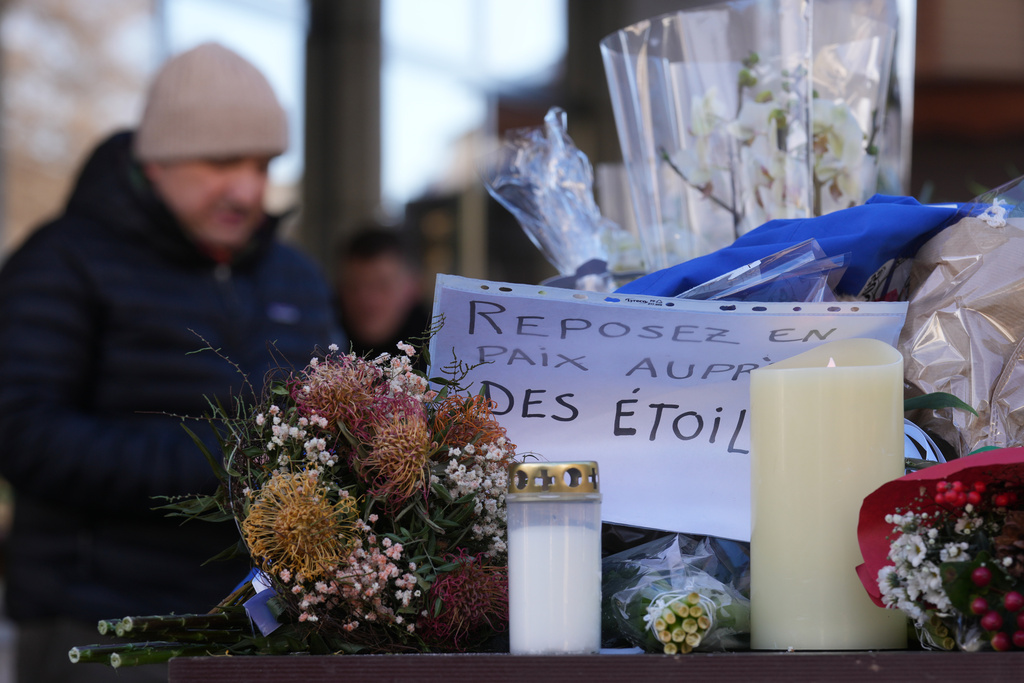 People bring flowers and letters, reading "Rest in Peace", near the sealed off Le Constellation bar, where a devastating fire left dead and injured during the New Year's celebrations in Crans-Montana, Swiss Alps, Switzerland, Friday, Jan. 2, 2026. (AP Photo/ Antonio Calanni)