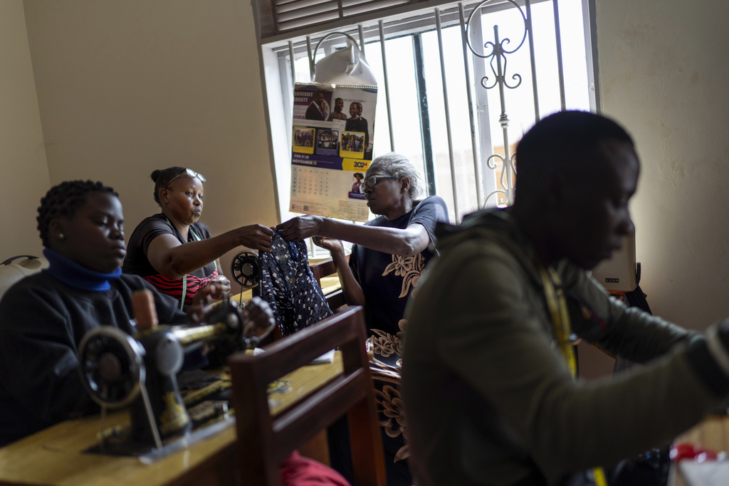 Lillian Ddungu, 68, right, teaches sewing to youth as part of a program by the NGO Health Nest Uganda, Monday, Nov. 25, 2024, in Entebbe, Uganda. The program helps both groups to share their skills with one another, from teaching youths how to sew and seniors learning about technology from the younger generation. (AP Photo/David Goldman)