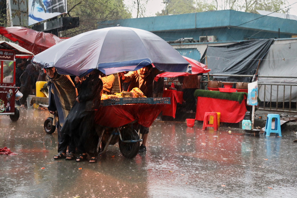 Residents take cover from heavy rain under the umbrella of a food stall at a market in Kabul, Afghanistan, Tuesday, March 31, 2026. (AP Photo/Siddiqullah Alizai)