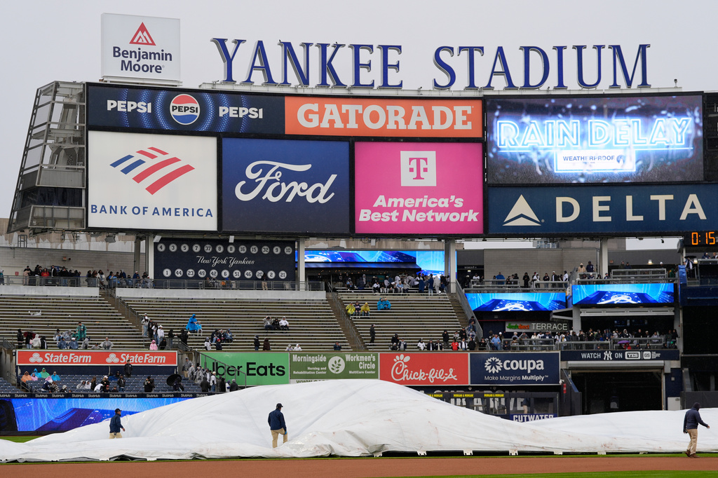 Members of the grounds crew take a tarp off the field during a rain delay before a baseball game between the New York Yankees and the Kansas City Royals, Sunday, April 19, 2026, in New York. (AP Photo/Seth Wenig)