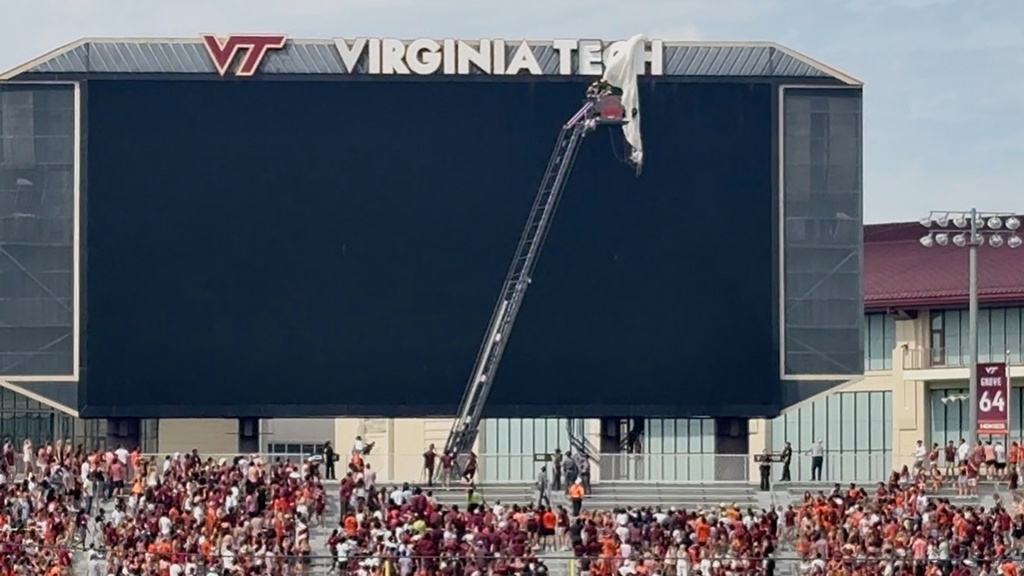 In this image from video, personnel on a lift work to secure a skydiver that crashed into the Lane Stadium scoreboard before Virginia Tech’s spring NCAA college football game, Saturday, April 18, 2026, in Blacksburg, Va. (Ben Walls/WRIC8 via AP)