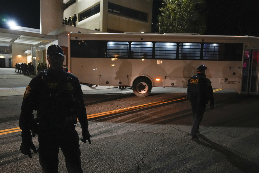 Law enforcement officers line the road outside a United States Immigration and Customs Enforcement (ICE) facility as a bus leaves with passengers on Tuesday, Oct. 21, 2025, in Portland, Ore. (AP Photo/Jenny Kane)