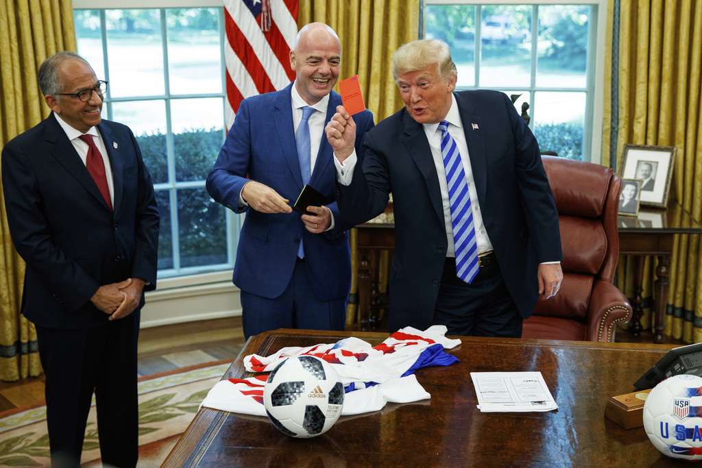 FILE - President Donald Trump holds up a red card during a meeting with FIFA president Gianni Infantino, center, and United States Soccer Federation president Carlos Cordeiro, left, in the Oval Office of the White House, Aug. 28, 2018, in Washington. (AP Photo/Evan Vucci, File)