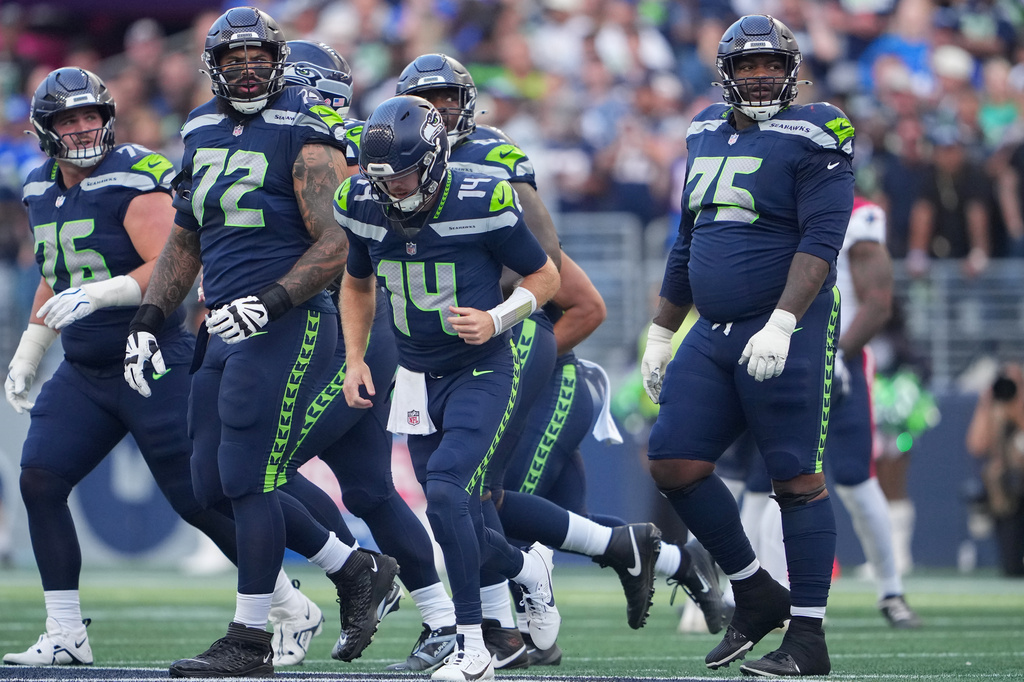 Seattle Seahawks quarterback Sam Darnold (14) is surrounded by guard Grey Zabel (76), tackle Abraham Lucas (72) and guard Anthony Bradford (75) after being sacked during the first half of an NFL football game against the New England Patriots, Wednesday, Sept. 9, 2026, in Seattle. (AP Photo/Lindsey Wasson)