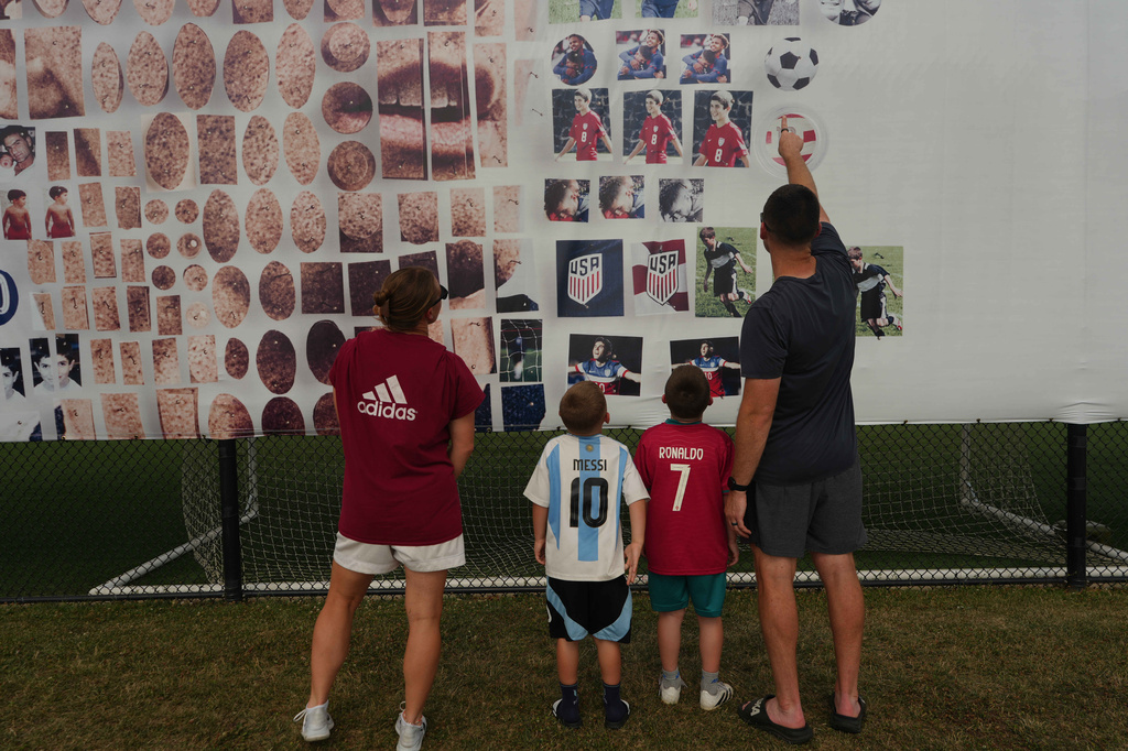 Pennsylvania Classic coaches, Brittney Jakobson, left, and Nick Jakobson, right, look at a banner of U.S. national team soccer player Christian Pulisic with their children, Declan Jakobson, who wears an Argentina jersey, and Camden Jakobson, wearing a Portugal jersey, at the club were Pulisic honed his skills in Manheim, Pa., on Monday, June 29, 2026. (AP Photo/Luis Andres Henao)