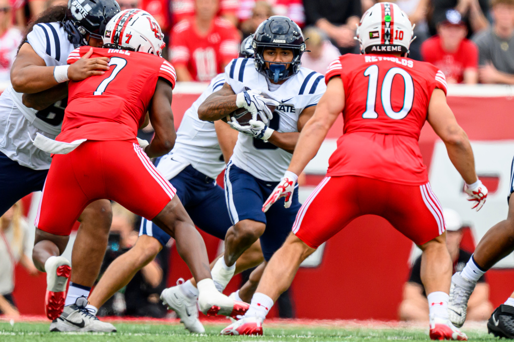 Utah State running back Javen Jacobs, center, runs the ball during the first half of an NCAA college football game against Utah, Saturday, Sept. 19, 2026, in Salt Lake City. (AP Photo/Tyler Tate)